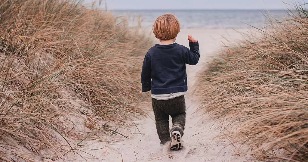 Niño caminando por un sendero de playa hacia el mar